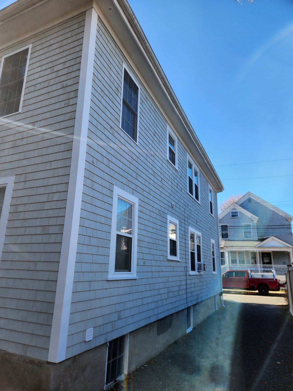 Light blue shingled house with white trim and windows on a clear day, with neighboring houses visible.