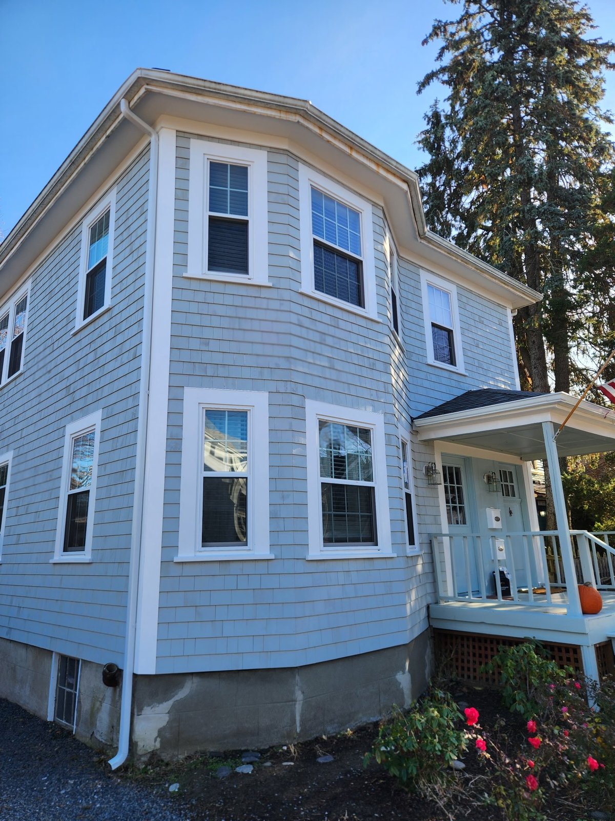 Blue and white two-story house with curved bay windows, front porch, and landscaping under clear sky.